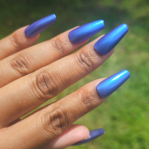 Petals and Poison Hand with blue nail polish against a blurred green background