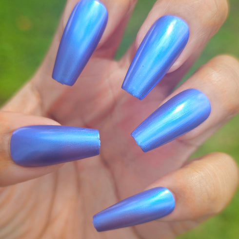 Petals and Poison Hand with blue nail polish against a blurred green background