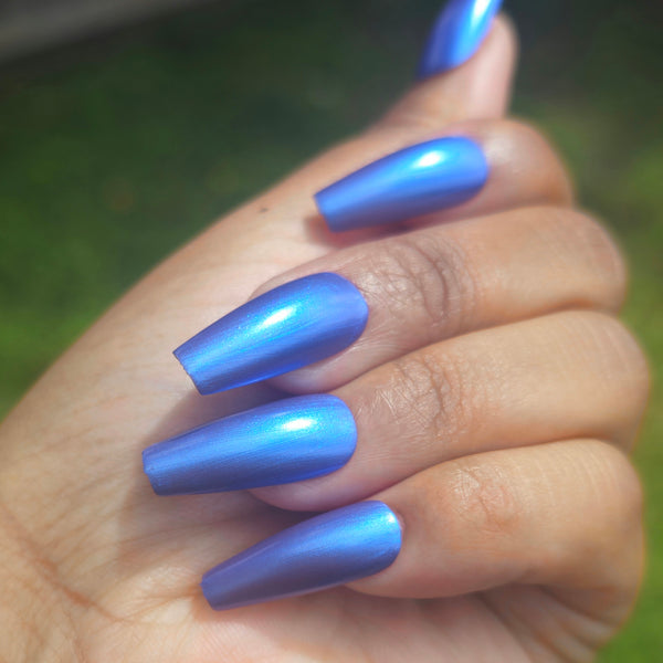 Petals and Poison  Hand with blue nail polish against a blurred green background