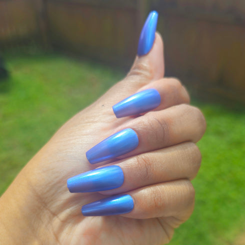 Petals and Poison Hand with blue nail polish giving a thumbs-up gesture outdoors.