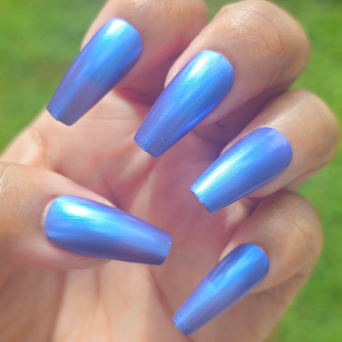 Petals and Poison Hand with blue nail polish against a blurred green background