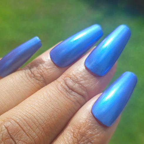 Petals and Poison Hand with blue nail polish against a blurred green background