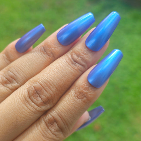 Petals and Poison Hand with blue nail polish against a blurred green background
